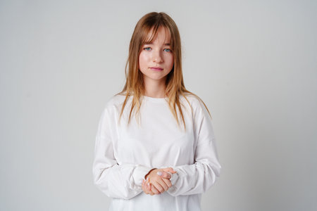 Teen girl stands in casual attire against a plain background, showcasing her thoughtful expressionの写真素材