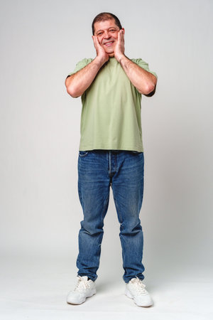 Happy middle-aged man showing joy while touching his face against a neutral backgroundの写真素材