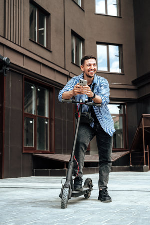 Young man enjoying a sunny day while riding an electric scooter through a modern urban settingの写真素材