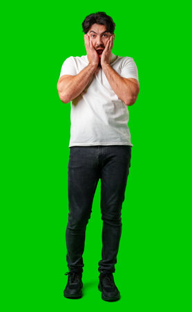 A man with a surprised expression holds his face while against a vibrant green backgroundの写真素材