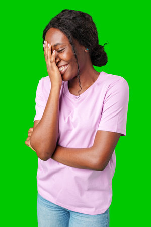 Happy young person laughing and playfully covering face while standing against a bright green backgroundの写真素材