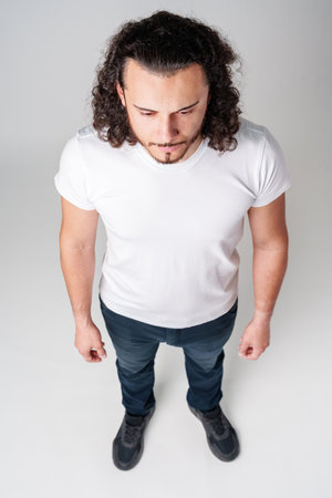 Man stands with a serious expression wearing a plain white shirt and dark jeans against a simple white backgroundの写真素材