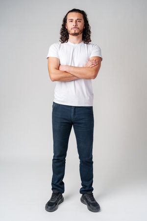 A confident young man with curly hair poses against a neutral backdropの写真素材