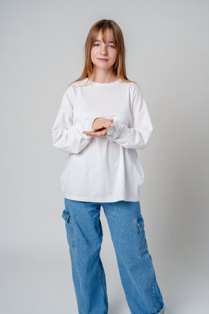 Casual indoor portrait of a young woman in a white sweater and blue jeans posing with her hands togetherの写真素材