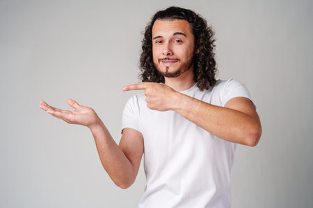Young man in a white t-shirt and jeans pointing confidently while smiling in a studio settingの写真素材