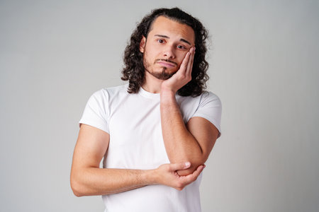 A young man stands thoughtfully against a plain backgroundの写真素材