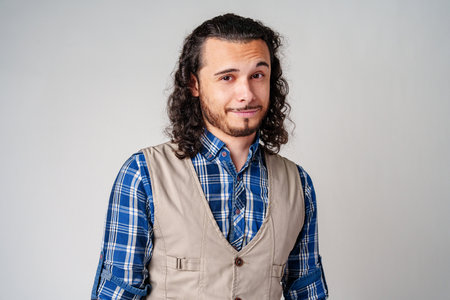Young man in plaid shirt and vest poses confidently against a neutral backgroundの写真素材