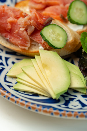 Colorful plate of smoked salmon sandwiches with cucumbers, greens, and olives on a decorative blue...