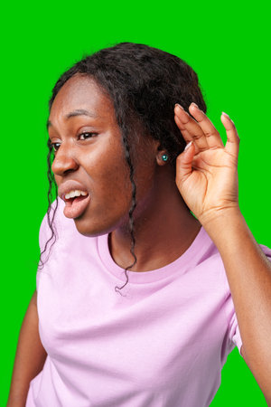 Young woman playfully listening with a smile against a vibrant green backgroundの写真素材