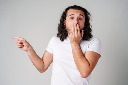 Young man in a white t-shirt and jeans pointing confidently in a studio settingの写真素材