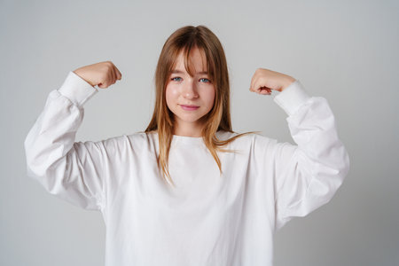 A joyful young girl with long hair wearing a white sweater stands against a plain backgroundの写真素材