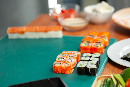 Freshly made sushi rolls with colorful vegetables sitting on a green cutting boardの写真素材