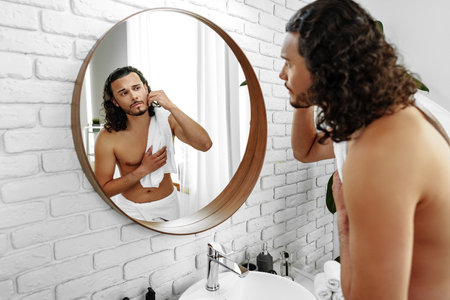 Young man grooming himself in a modern bathroom mirror with natural lightingの写真素材