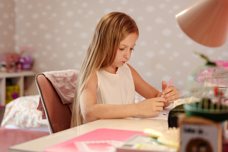 A young girl sits at her desk in her bedroom, focusing intently on a drawingの写真素材