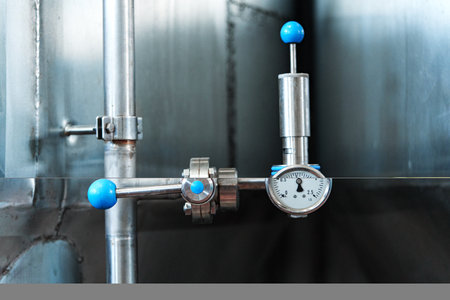 A close-up of a pressure gauge and valve attached to a pipe in a factory setting