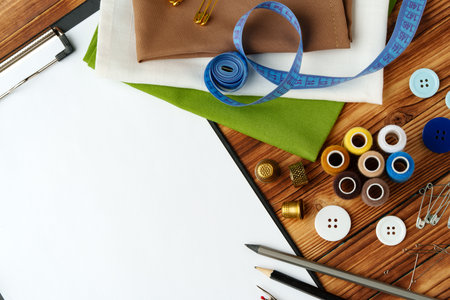 Colorful sewing supplies arranged around a blank clipboard on a wooden table