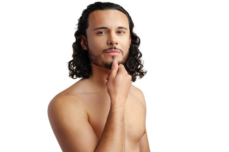 Young man with curly hair thoughtfully posing against a plain backgroundの写真素材