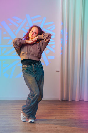 A young woman dances in a studio, her pose illuminated by a colorful geometric projection