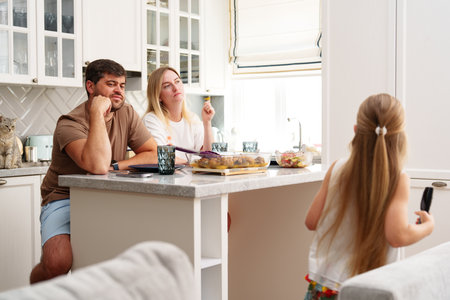 A young girl walks away from her parents who are sitting at the kitchen counterの写真素材