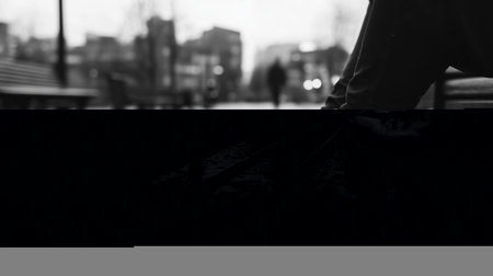 Person sitting on a wet park bench wearing white sneakers during a rainy day in an urban environmentの素材