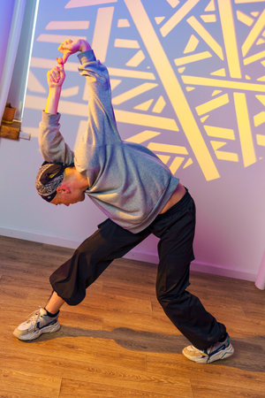 A dancer stretches in a studio with a colorful light projection on the wall