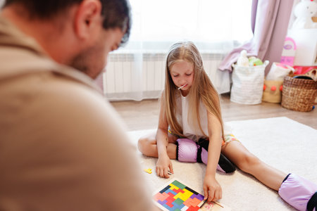 A young girl plays a puzzle game with her father on a carpet in their homeの写真素材