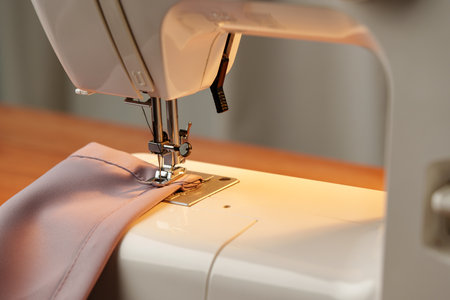 Sewing machine in use on a wooden table, stitching a light fabric in a well-lit indoor workspace