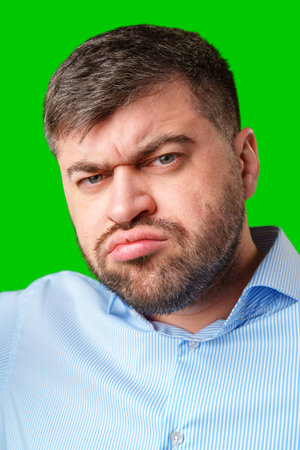 A man with a serious expression wearing a light blue shirt poses against a bright green backgroundの写真素材