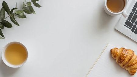 Breakfast setting with tea, croissant, and laptop on white table in cozy workspaceの素材