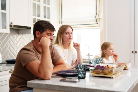A family sits at the kitchen table, eating a meal, but the mood seems tenseの写真素材