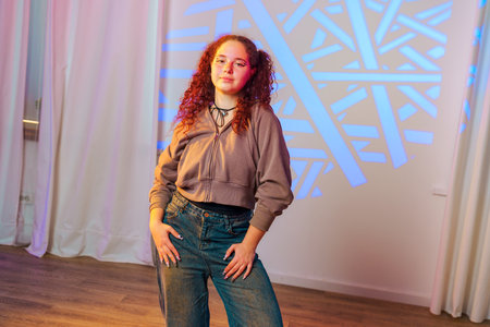 A young woman with red curly hair stands in front of a wall with a blue light projection