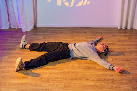 A person is lying on a wooden floor with their arms outstretched and eyes closed, as if they are...