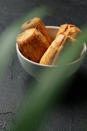 Delicious freshly baked pastries resting in a bowl surrounded by greenery on a dark background