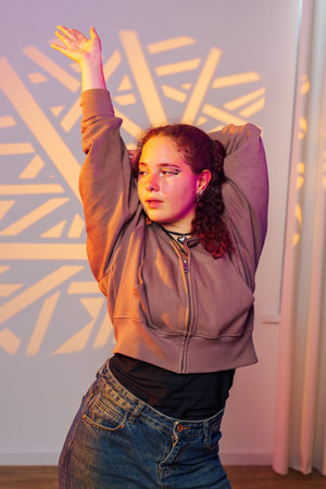 A young woman with curly hair poses in a studio, illuminated by colorful lights