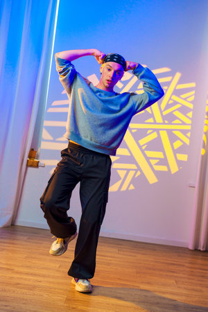 A young man dances in a studio, his movements accentuated by the colorful lights and geometric patterns projected on the wallの写真素材