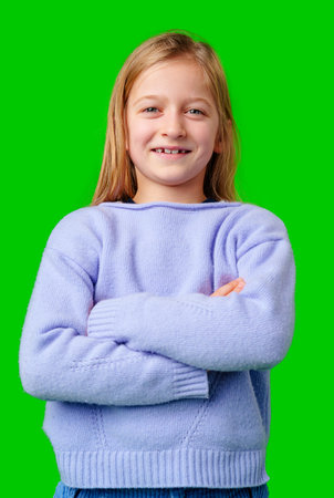 Child wearing a blue sweater and light blue pants stands confidently in front of a green backgroundの写真素材