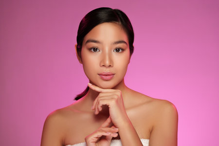 Young woman posing with a thoughtful expression against a pink background during a beauty photoshootの写真素材