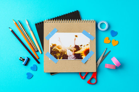 Creative workspace with scrapbook tools and a joyful photo resting on a bright blue surfaceの写真素材