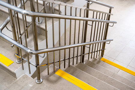Safety railing guides the path down the staircase in a modern building with yellow warning lines on the stepsの写真素材