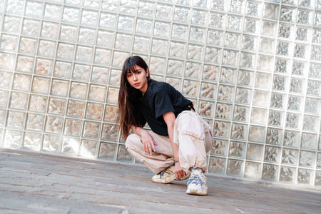 Young dancer poses in urban setting with glass brick wall during daylight hoursの写真素材