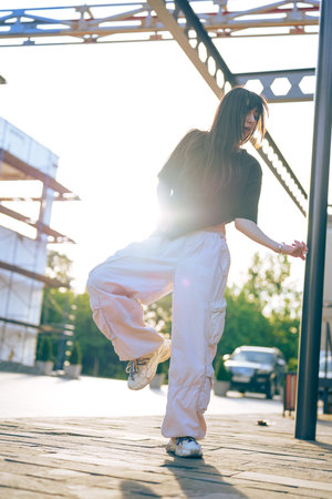 Young woman dancing gracefully outdoors during golden hour against a backdrop of construction