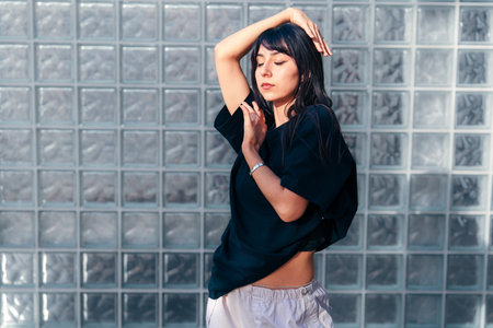 Woman gracefully dancing in a minimalist space with glass block wall in the background during a sunny afternoonの写真素材