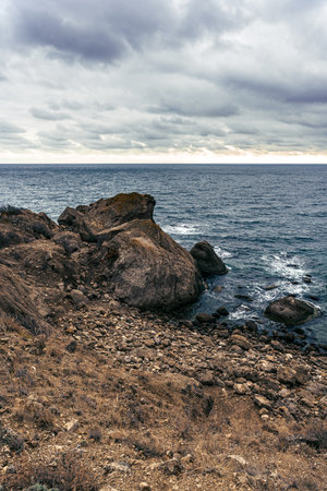 Cloudy skies over rocky coastline with waves crashing on shore at dusk near the ocean