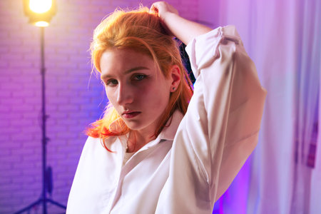 Young woman posing confidently in a stylish outfit with colorful lighting in a modern indoor settingの写真素材