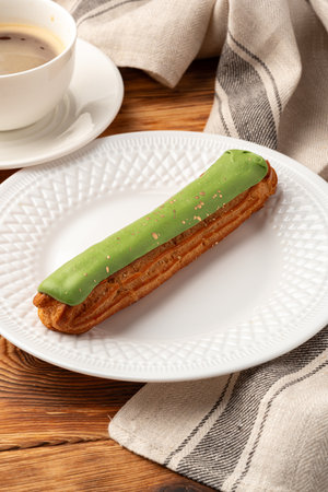 Delicious matcha eclair served on a white plate next to a cup of coffee at a cozy cafe