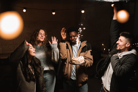 Celebration with friends as they joyfully raise their hands around a festive cake with sparklers at...