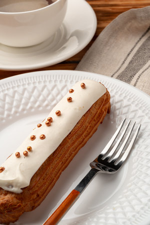 Delicious pastry with cream topping and golden sprinkles served next to a cup of coffee on a wooden...