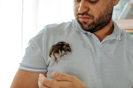 Man interacting with a small hamster on his shoulder in a cozy indoor settingの写真素材