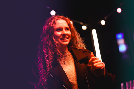 Woman smiles in vibrant night setting while enjoying a lively outdoor gathering with colorful lights...