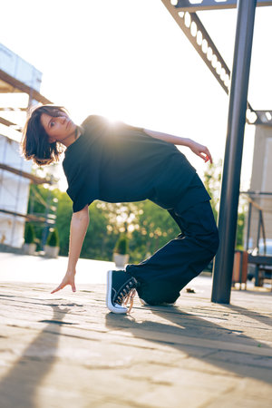 Young dancer performs dynamic pose outdoors during golden hour in urban environment